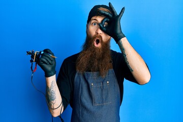 Redhead man with long beard tattoo artist wearing professional uniform and gloves doing ok gesture...