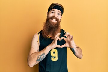 Redhead man with long beard wearing basketball uniform smiling in love doing heart symbol shape with hands. romantic concept.