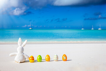 Easter travel concept with a bunny and colorful eggs sitting on a tropical paradise beach