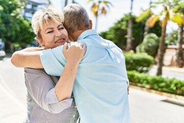 Middle age caucasian couple of husband and wife together on a sunny day outdoors. Smiling happy in love hugging at the city.