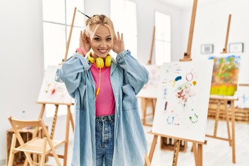 Young caucasian girl at art studio trying to hear both hands on ear gesture, curious for gossip. hearing problem, deaf
