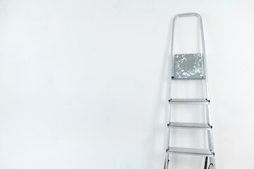Folding aluminum staircase in an empty room on a white wall background.