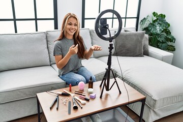 Young caucasian girl making makeup tutorial sitting on the sofa at home. - obrazy, fototapety, plakaty