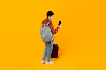 Tourist Guy Using Smartphone Standing With Luggage Over Yellow Background