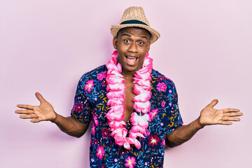 Young black man wearing summer shirt and hawaiian lei celebrating victory with happy smile and winner expression with raised hands - obrazy, fototapety, plakaty