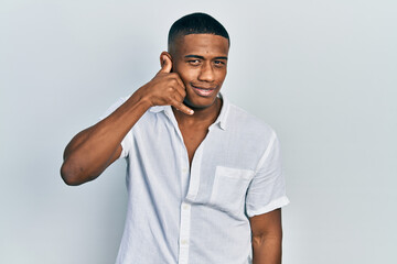 Young black man wearing casual white shirt smiling doing phone gesture with hand and fingers like talking on the telephone. communicating concepts.