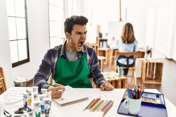 Young artist man at art studio angry and mad screaming frustrated and furious, shouting with anger. rage and aggressive concept. © Krakenimages.com