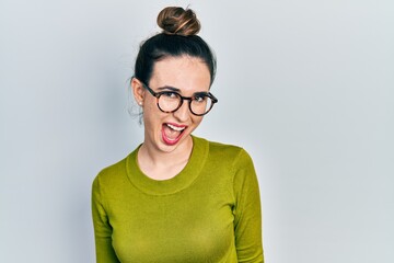 Young hispanic girl wearing casual clothes and glasses winking looking at the camera with sexy expression, cheerful and happy face.