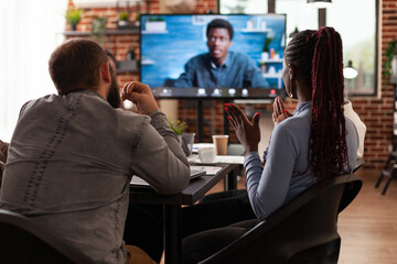 Group of businesspeople working at company presentation discussing strategy ideas with remote manager during online videocall meeting conference in startup office. Business call on computer monitor