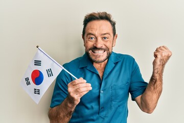 Middle age man holding south korea flag screaming proud, celebrating victory and success very excited with raised arm