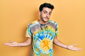Young hispanic man wearing casual clothes clueless and confused expression with arms and hands...