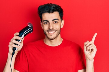Young hispanic man charging electric razor machine smiling happy pointing with hand and finger to...