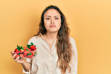 Young hispanic girl holding strawberries depressed and worry for distress, crying angry and afraid. sad expression.