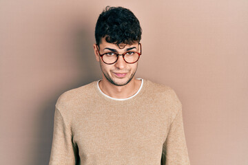 Young hispanic man wearing casual clothes and glasses skeptic and nervous, frowning upset because...