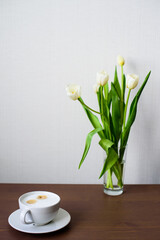 A bouquet of white tulips and a coffee cup on the table