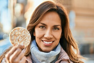 Young hispanic woman smiling happy holding rice cake at the city.