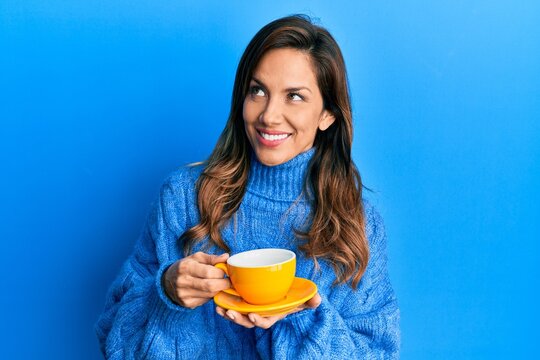 Young latin woman drinking a cup of coffee smiling looking to the side and staring away thinking.
