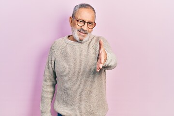 Handsome senior man with beard wearing casual sweater and glasses smiling friendly offering handshake as greeting and welcoming. successful business.