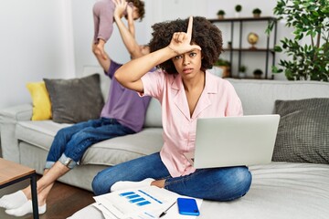 Mother of interracial family working using computer laptop at home making fun of people with fingers on forehead doing loser gesture mocking and insulting.