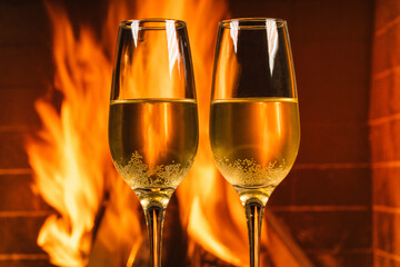 Two glasses of champagne before a cozy burning fireplace in country house.