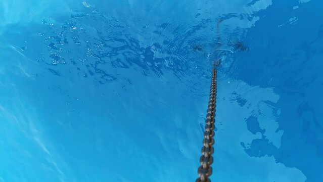 Vertical shot of ship anchor rising up from underwater is filmed from above. Heavy iron hook on metal chain is moving up from the blue sea. Concept of transportation by vessels. Concept of watercraft.