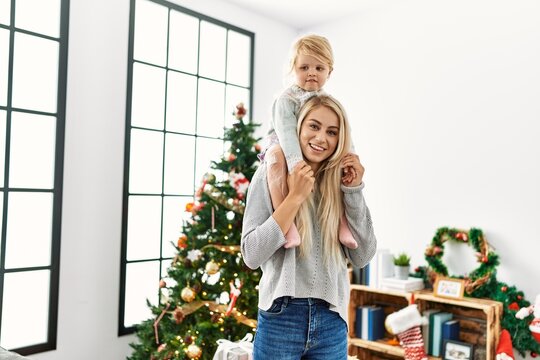 Mother and daughter holding child on shoulders standing by christmas tree at home