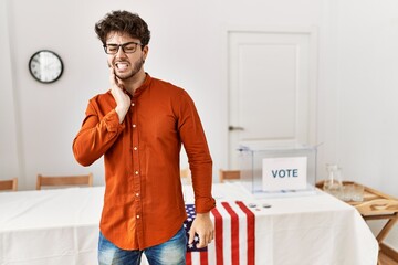 Hispanic man standing by election room touching mouth with hand with painful expression because of...