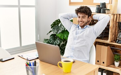 Young hispanic businessman relaxed with hands on head at the office.