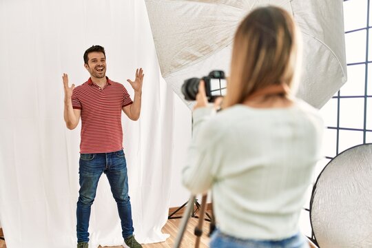 Woman photographer talking pictures of man posing as model at photography studio celebrating victory with happy smile and winner expression with raised hands