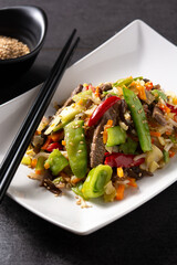 Beef, vegetables and sesame seeds in white plate on black background