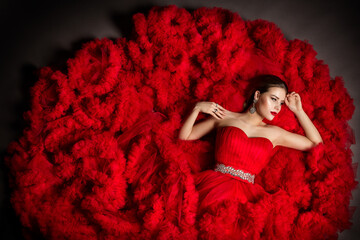 Fashion Model in Red Fluffy Cloud Dress lying down. Beauty Woman Portrait with Silver Jewelry....