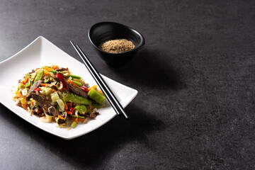 Beef, vegetables and sesame seeds in white plate on black background. Copy space
