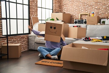 Young african american woman sitting on the floor with funny cardboard box on head at new home