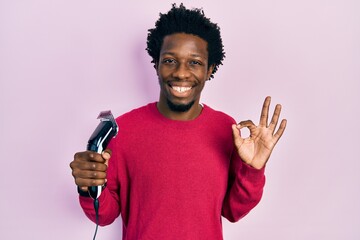 Young african american man holding razor doing ok sign with fingers, smiling friendly gesturing excellent symbol