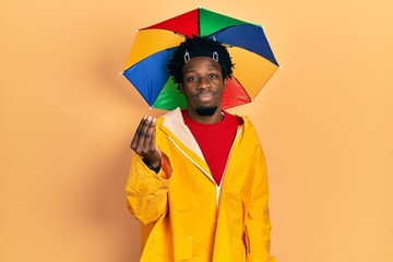Young african american man wearing yellow raincoat doing italian gesture with hand and fingers...