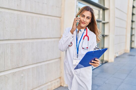 Young blonde woman wearing doctor uniform talking on the smartphone at hospital