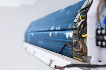 the bare indoor unit of air conditioner reveals blue aluminum fins, copper pipes and wires during annual cleaning.