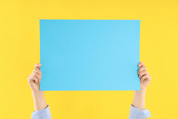 Female hands hold blank banner on yellow background