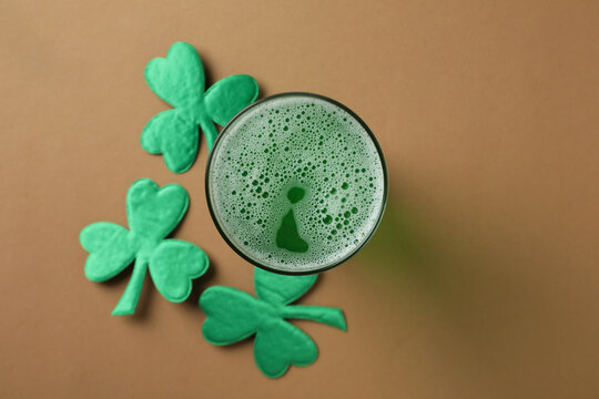 Glass of ale and clover leaves on beige background