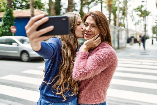 Mother and daughter hugging each other and kissing making selfie by the smartphone at street