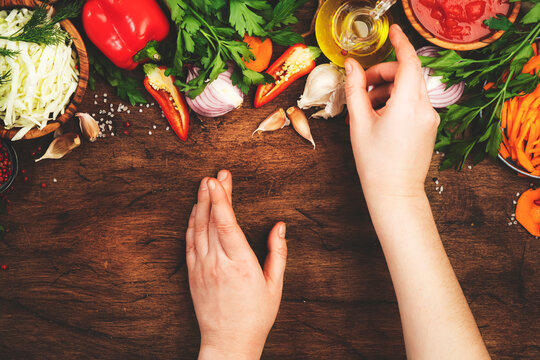 Fresh vegan vegetarian ingredients, vegetables, spices, herbs for healthy eating on rustic wooden kitchen table with cutting board. Womens hands takes oil bottle. Diet, clean, comfort food 