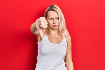 Beautiful caucasian blonde woman wearing casual white t shirt looking unhappy and angry showing rejection and negative with thumbs down gesture. bad expression.