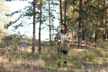 cute girl with dark long hair in glasses looks down standing in the forest with a backpack