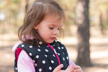 A beautiful little girl in a polka dot vest on a walk in the forest touches her hands