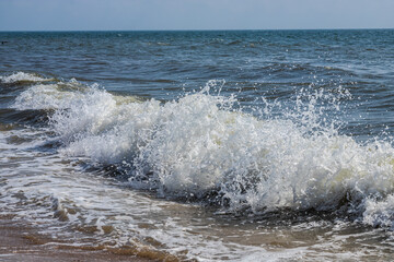 Sea waves crash against large rocks on the shore, forming large splashes