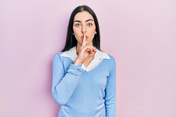 Beautiful woman with blue eyes standing over pink background asking to be quiet with finger on lips. silence and secret concept.