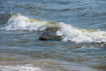 Sea waves crash against large rocks on the shore, forming large splashes