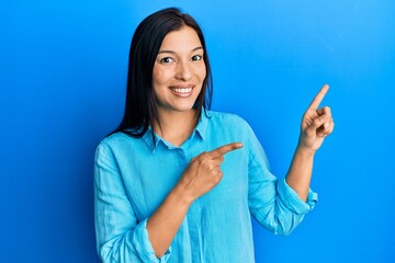 Young latin woman wearing casual clothes smiling and looking at the camera pointing with two hands and fingers to the side.