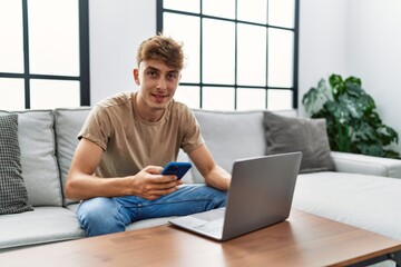 Young caucasian man smiling confident using laptop and smartphone at home