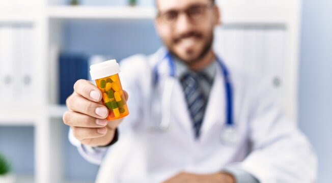 Young hispanic man wearing doctor uniform holding pills at clinic